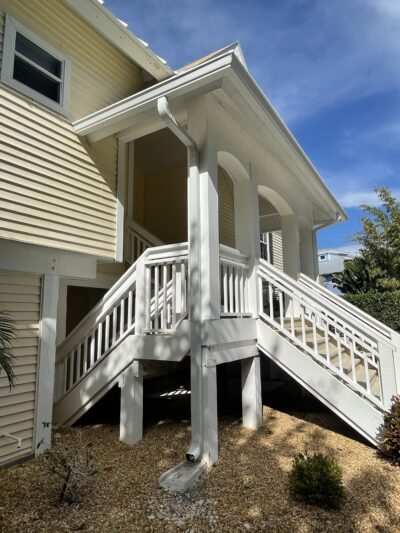 White Rain Gutter System Directing Water Flow From An Elevated Porch Of A Yellow House In Fort Myers.