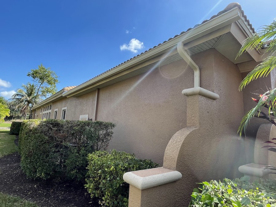 Seamless Rain Gutters Installed On A Beige Stucco House With Landscaped Bushes And Clear Blue Sky In Fort Myers.